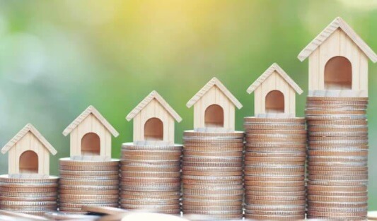 Model wooden houses sitting atop stacked coins in a fashion to indicate gowing investments.